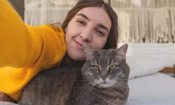 Vrouw in een geel vest neemt selfie met grijze kat